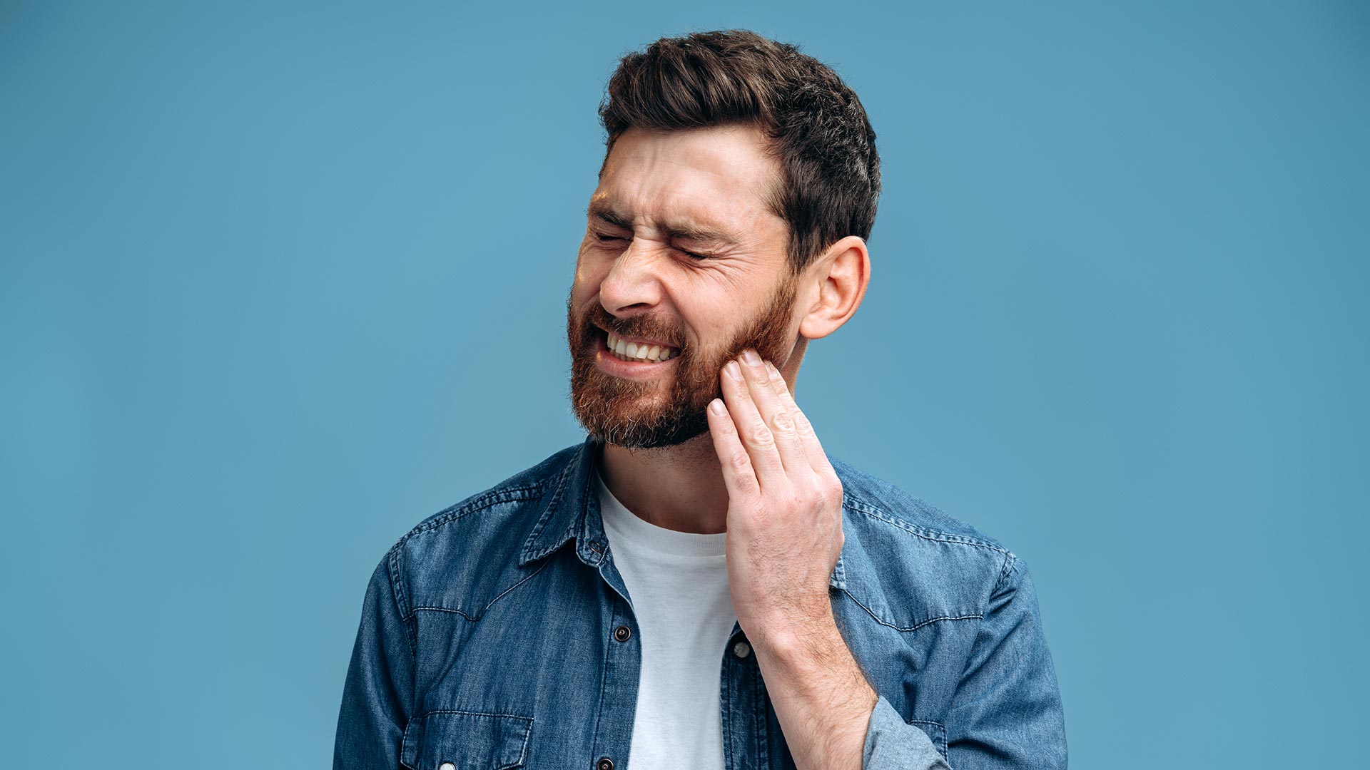 man holding cheek experiencing tooth pain